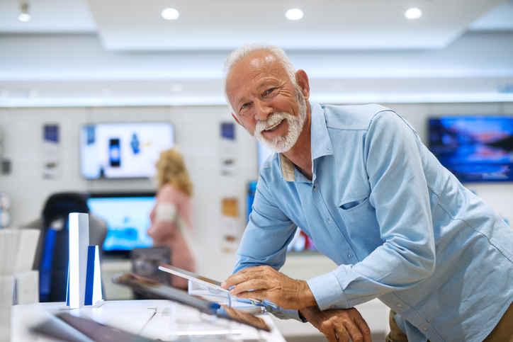 Senior bearded man looking at camera and trying out tablet while leaning on stand.